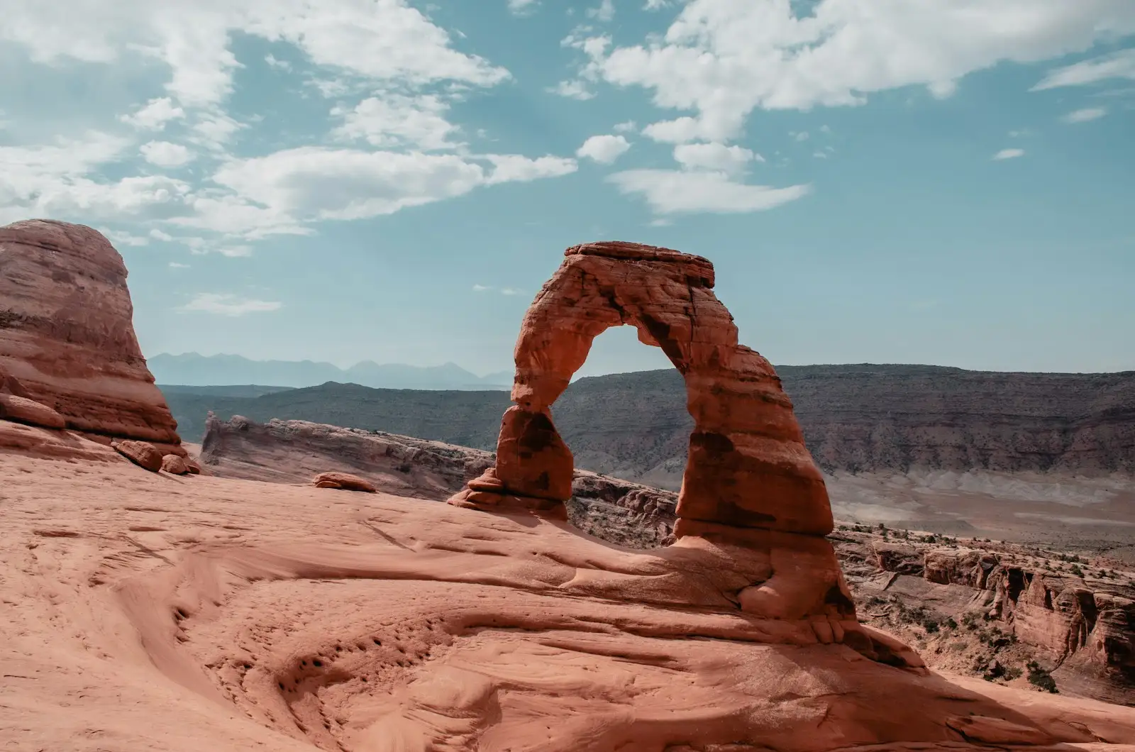 A person seated on red sandstone beneath Delicate Arch in Arches National Park near Moab, Utah.
